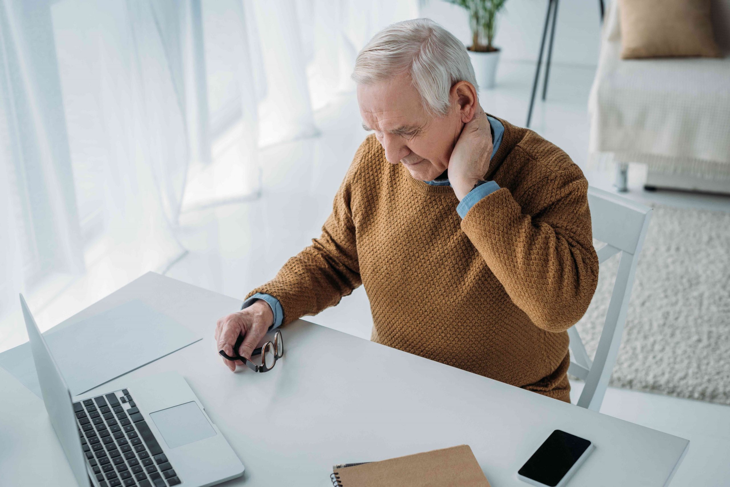 Senior man working in office and suffering from pain in neck