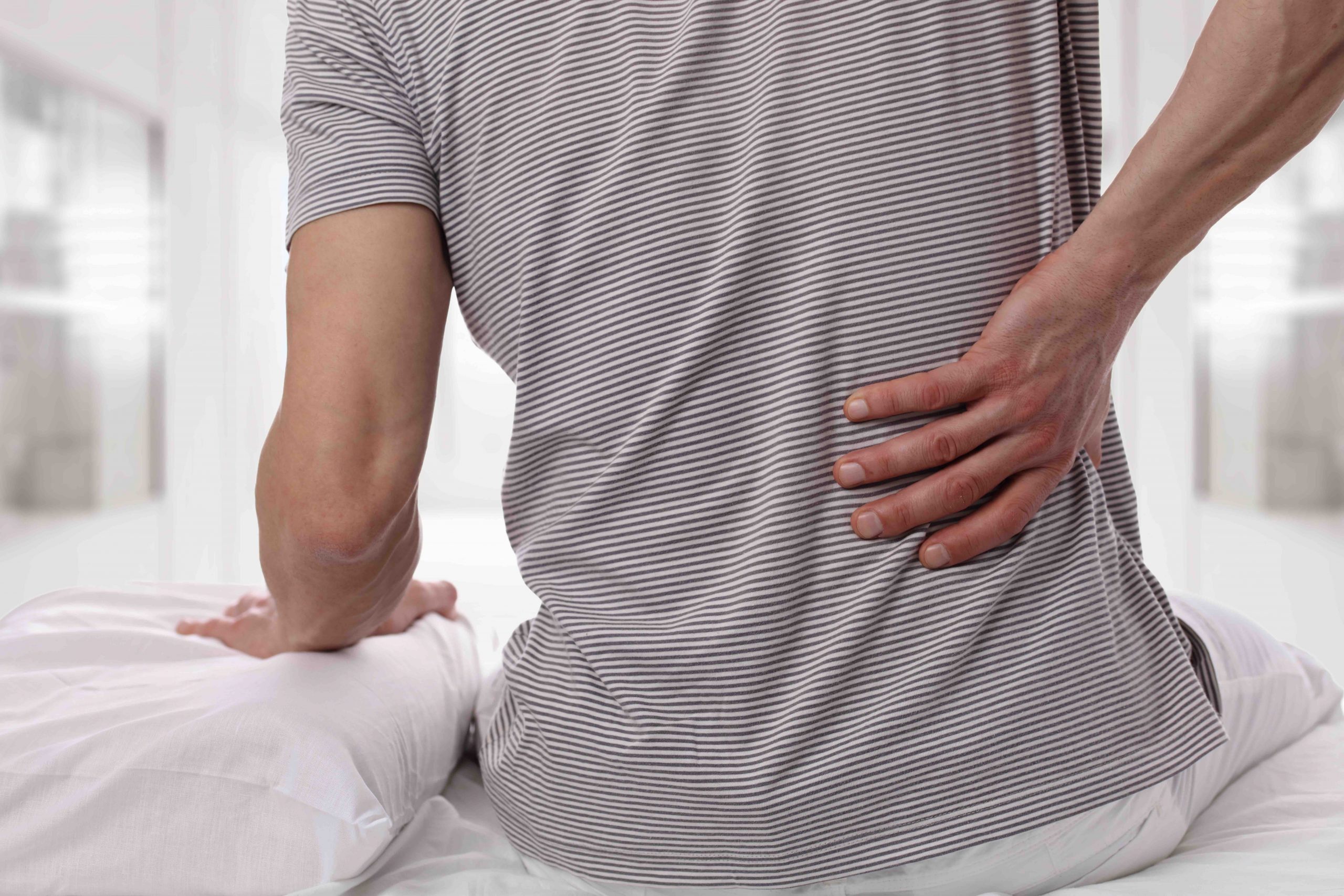 Man suffering from back pain at home in the bedroom. Uncomfortable mattress and pillow causes back pain. treat back pain with VCF